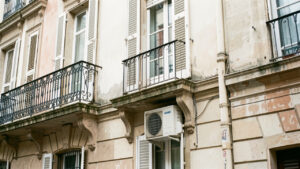 Façade d’un ancien immeuble français avec une unité extérieure de climatisation intégrée discrètement sous une fenêtre.